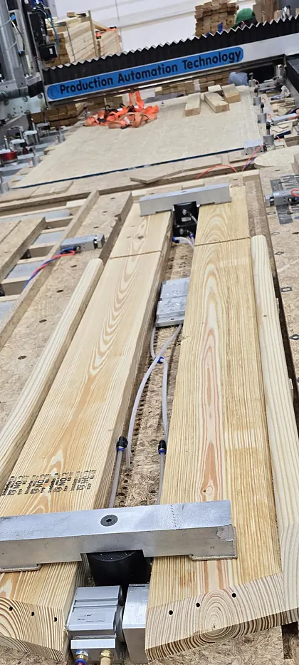 Long wooden fixture with pneumatic clamps on the CNC router table, under the Production Automation Technology gantry