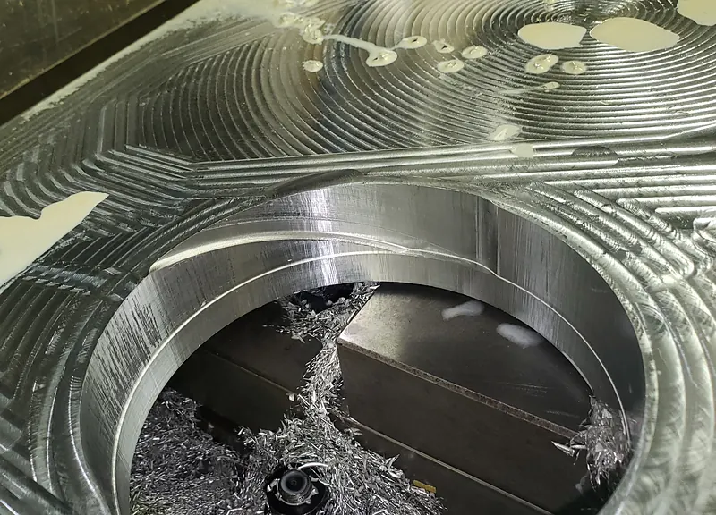 Large machined aluminum part with a circular pocket and a fine toolpath finish, wet with coolant
