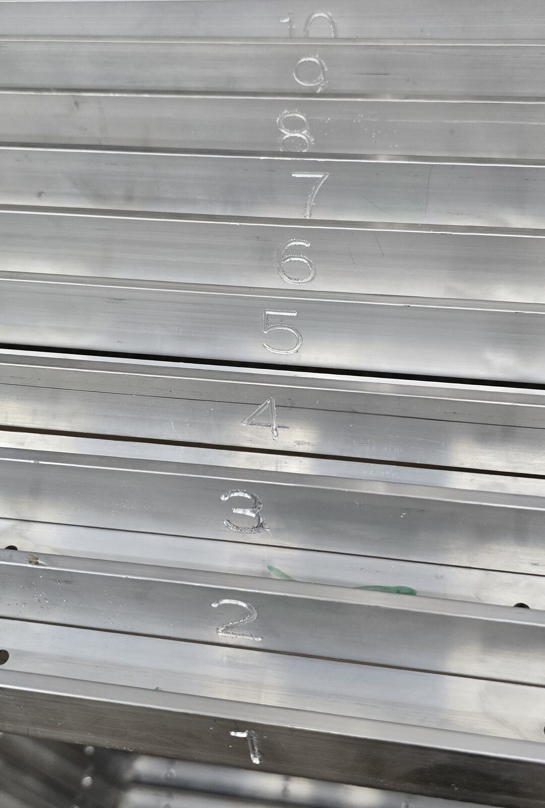 Stack of aluminum channel parts CNC-engraved with sequence numbers 1 through 10
