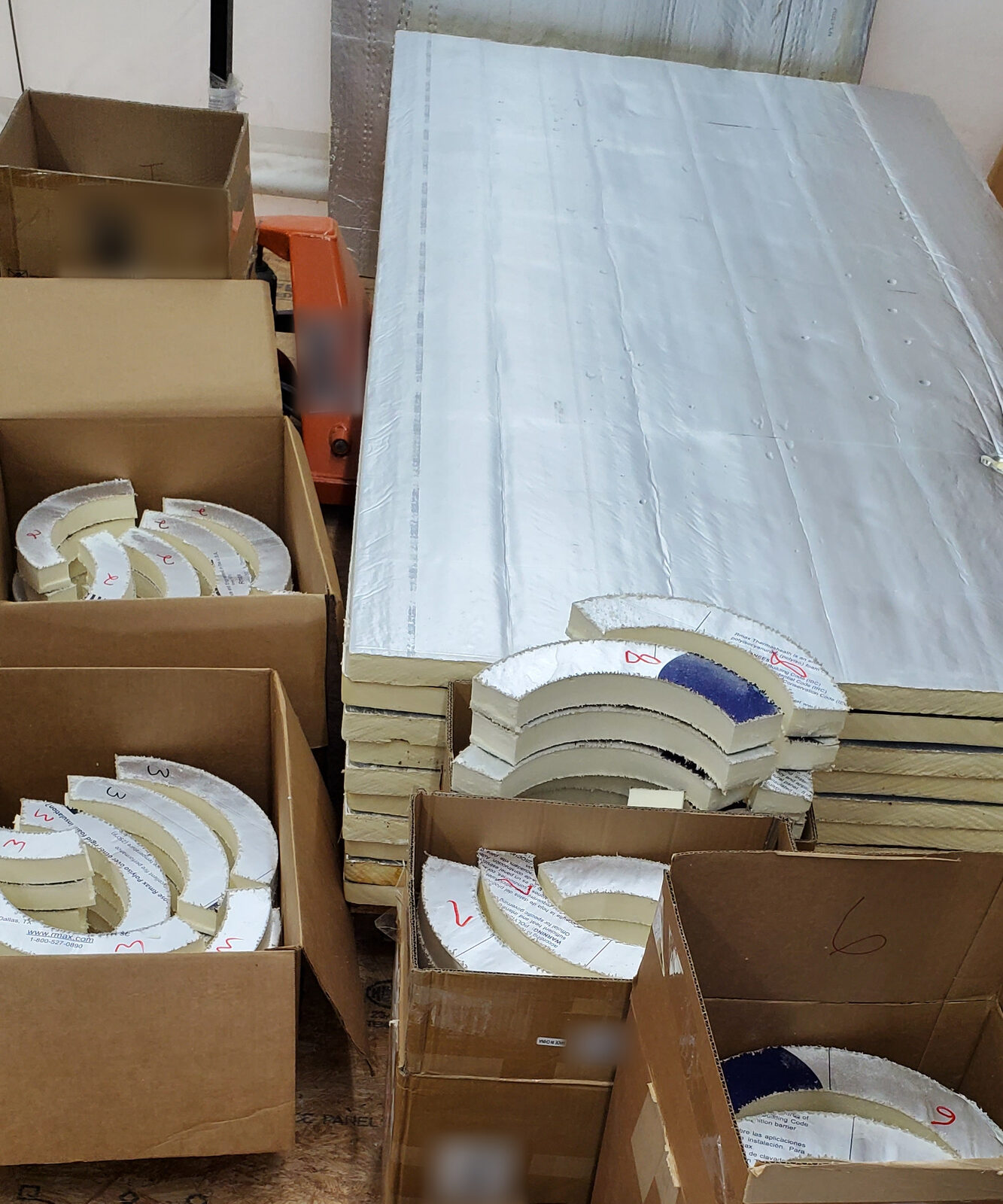 Boxed curved polyiso foam insulation pieces, each numbered for assembly, next to a stack of full sheets