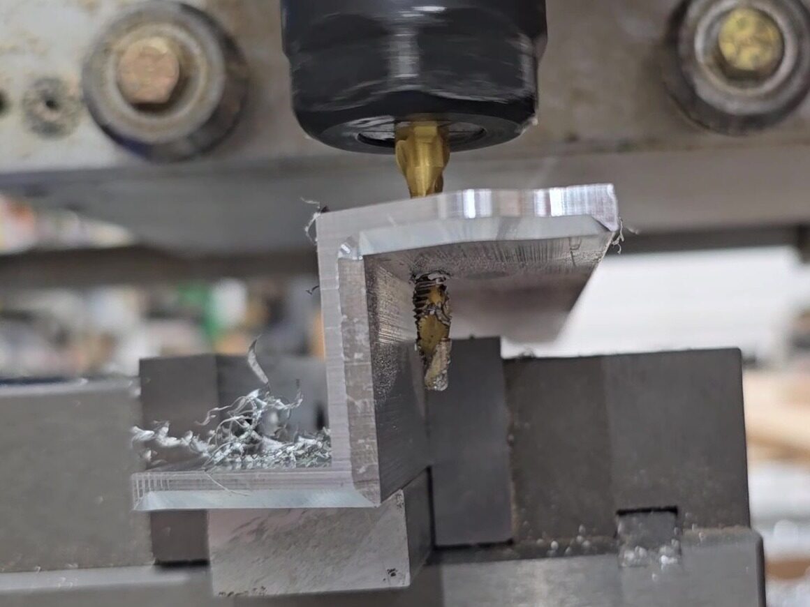 Spiral tap rigid-tapping a hole in an aluminum angle held in a vise, with chips